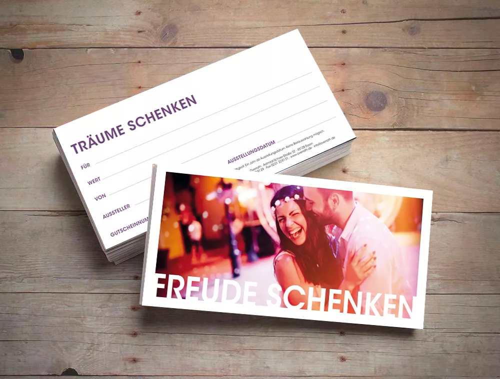 Ein maßgeschneiderter Gutschein der Tanzschule Overrath in Essen liegt auf Holz, daneben Karten mit den Sprüchen Träume schenken und Freude schenken.